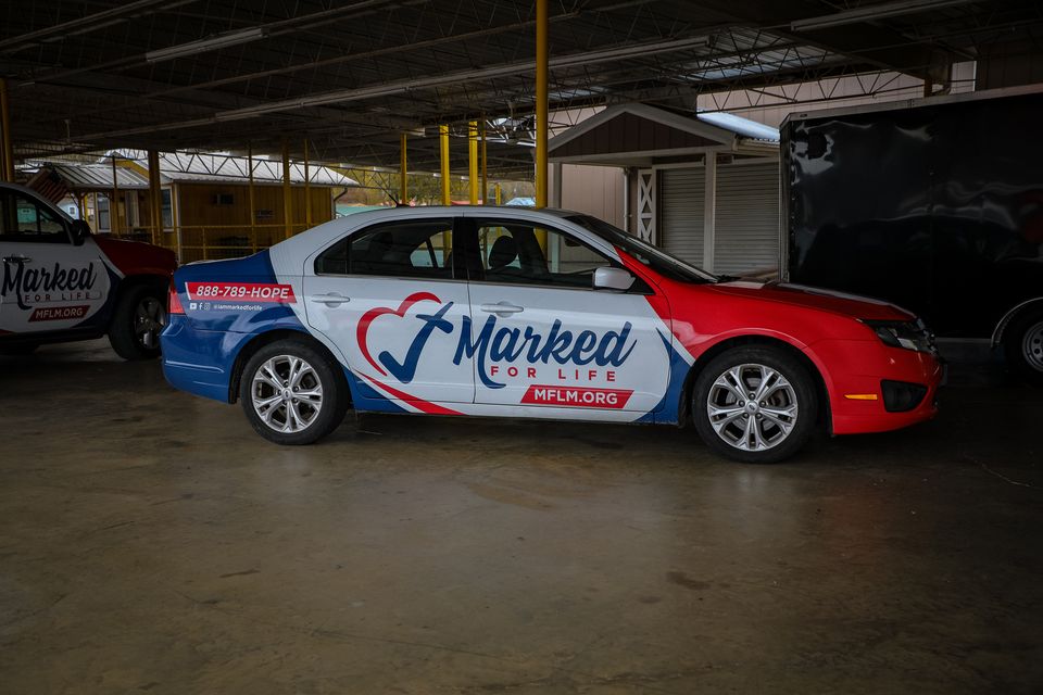 The Marked For Life car, wrapped in red, white, and blue with the 888-789-HOPE number, parked under a pavilion.
