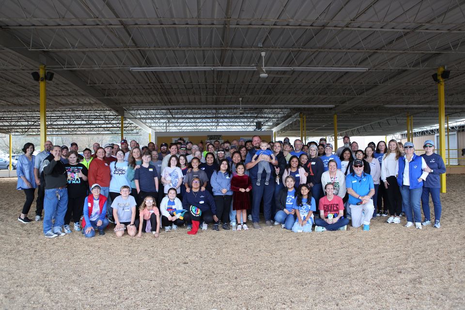 Dozens of neighbors and volunteers gather for a group photo under the pavilion after a community meal.