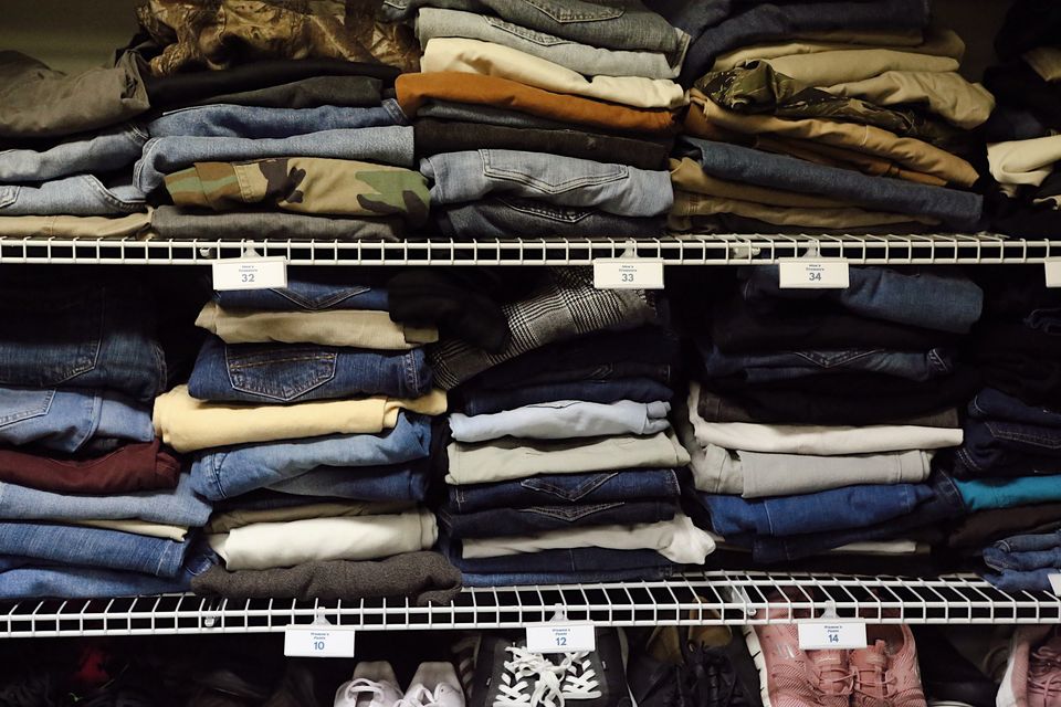 Folded jeans and pants sorted by waist size on wire shelves in the Hope Center clothing closet.
