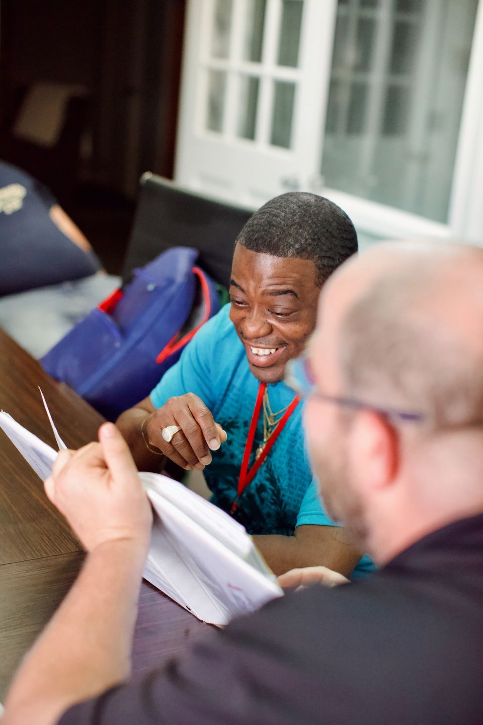 A neighbor in a bright blue shirt laughs while a case manager reviews paperwork with him at a table.