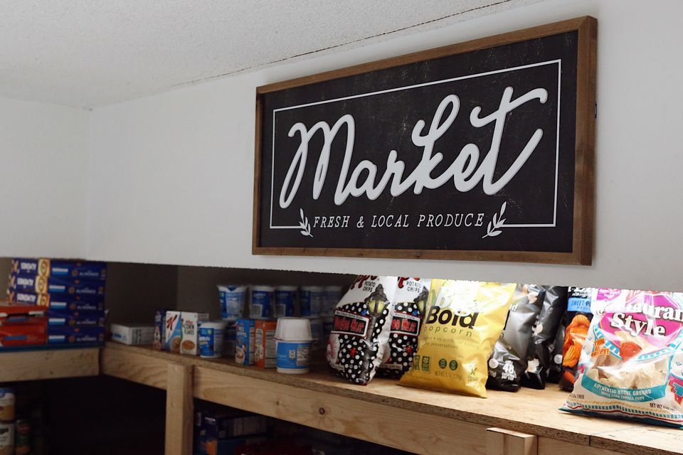 A chalkboard sign reading Market, Fresh and Local Produce, above shelves of snacks in the Hope Center.