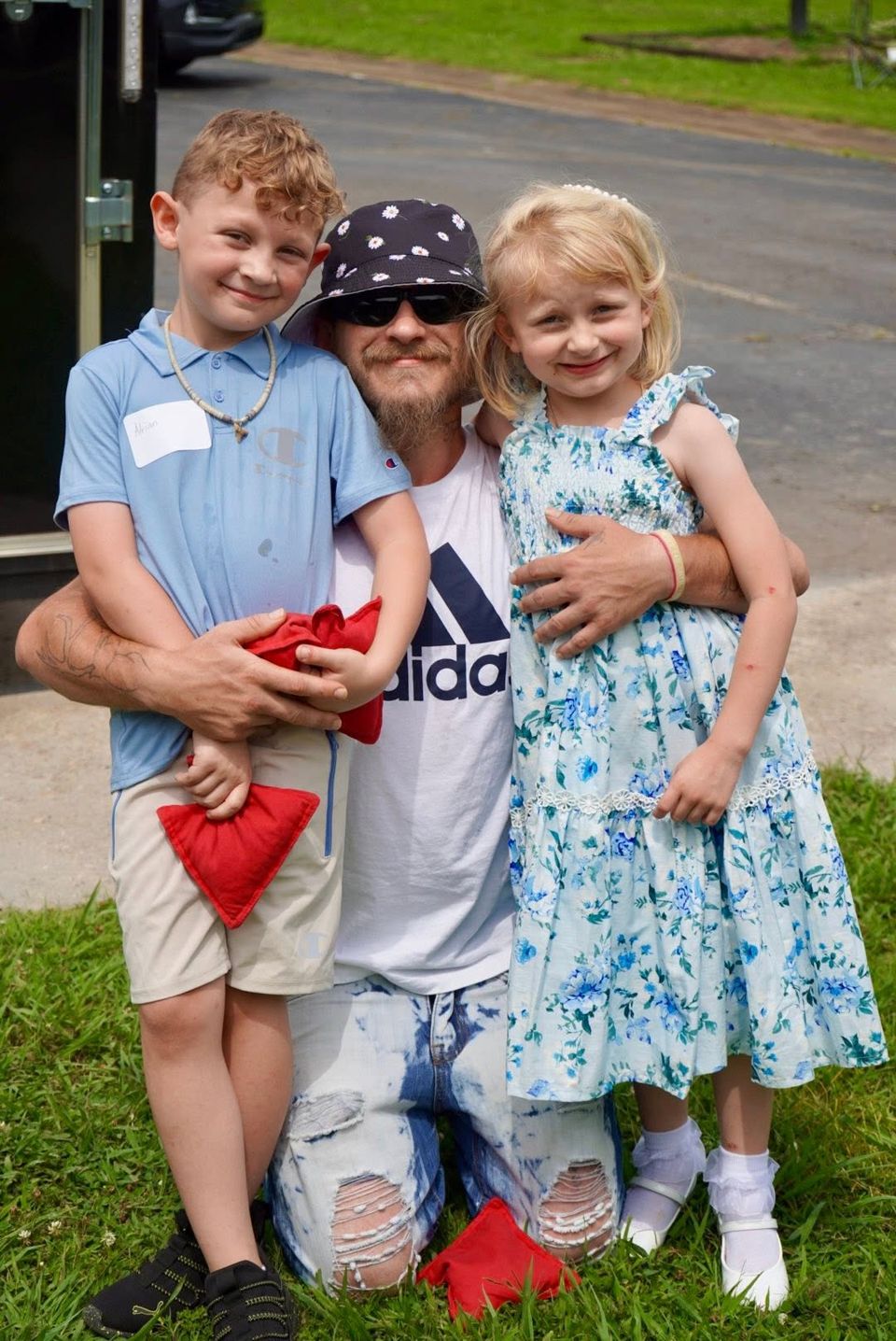 A Hope House student kneels in the grass with his two children on family day.