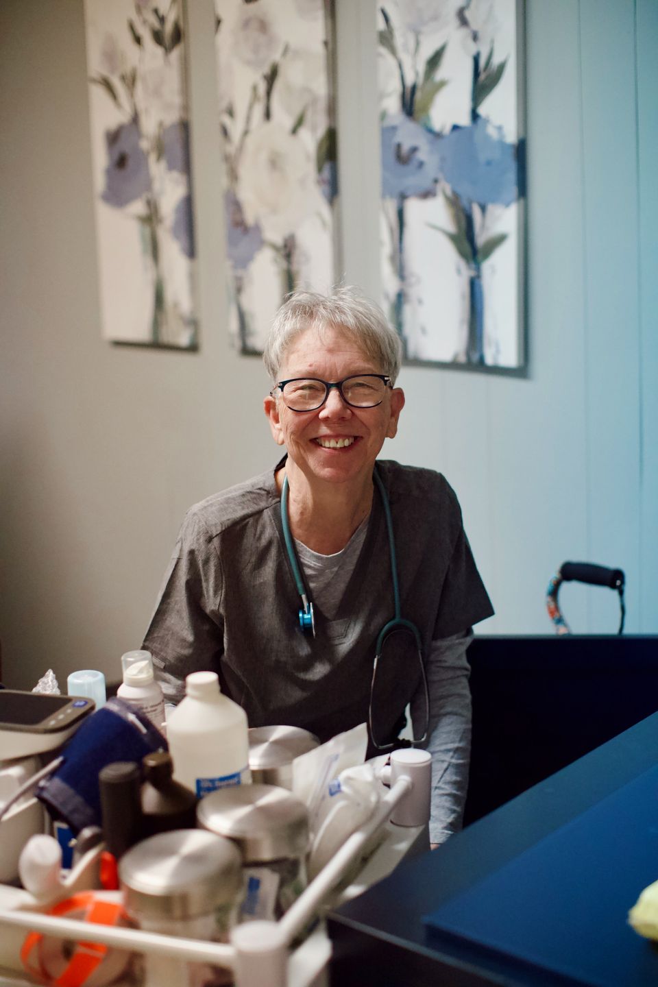 A nurse in grey scrubs with a teal stethoscope smiles beside a supply cart at the Marked For Life Medical Center.