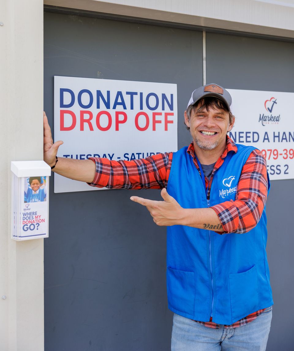 A Thrift Store team member in a blue vest points to the Donation Drop Off sign at the loading bay door on 15th Street.