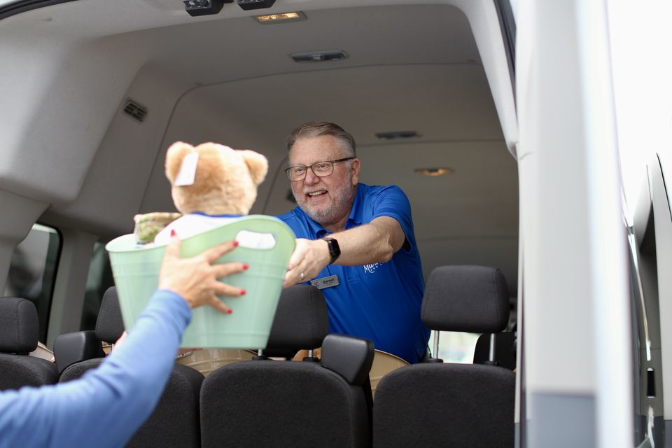 Darrell, a volunteer in a blue Marked For Life polo, hands a basket with a teddy bear and blankets out of a van.
