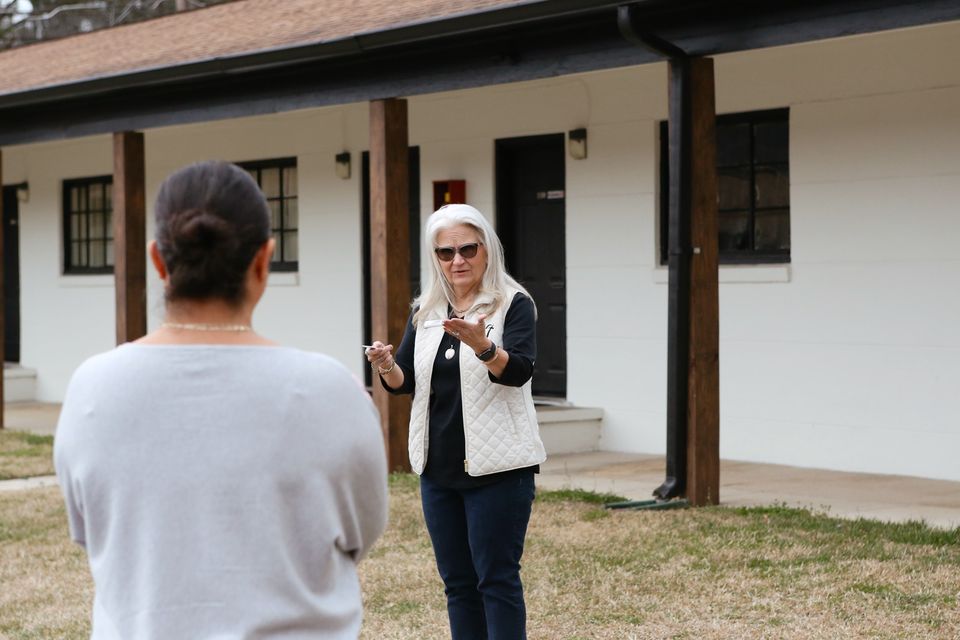 A staff member in a white vest gestures while talking with a new volunteer outside the Hope House.